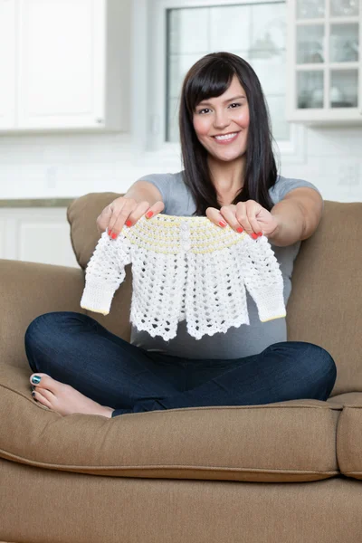 Schwangere hält Babykleidung auf Sofa — Stockfoto