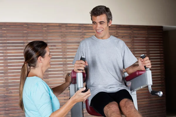 Homem usando uma máquina de exercício enquanto olha para o instrutor — Fotografia de Stock