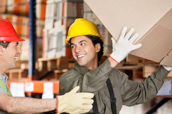 Foreman met collega opheffing kartonnen doos in magazijn — Stockfoto