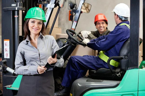 Säker kvinnliga handledare med truckföraren på lager — Stockfoto