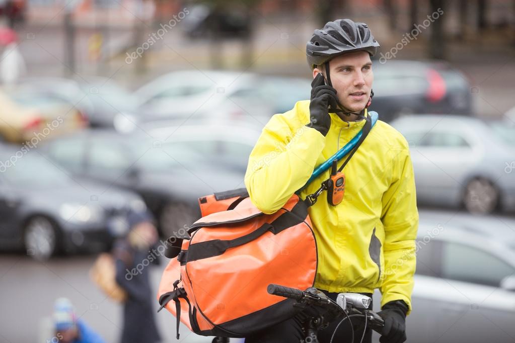 Male Cyclist With Courier Bag Using Mobile Phone On Street Stock Photo