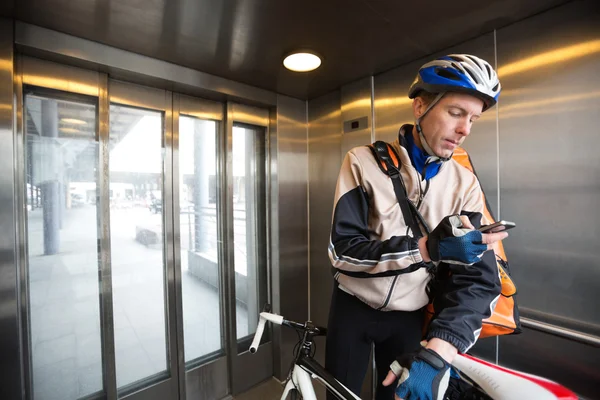 Manlig cyklist med courier påse med mobiltelefon i en hiss — Stockfoto