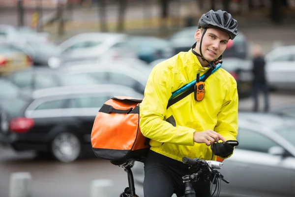 Ciclista masculino com saco de correio usando telefone celular na rua — Fotografia de Stock