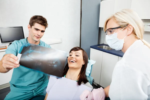 Dentista con assistente femminile che mostra l'immagine a raggi X al paziente — Foto Stock