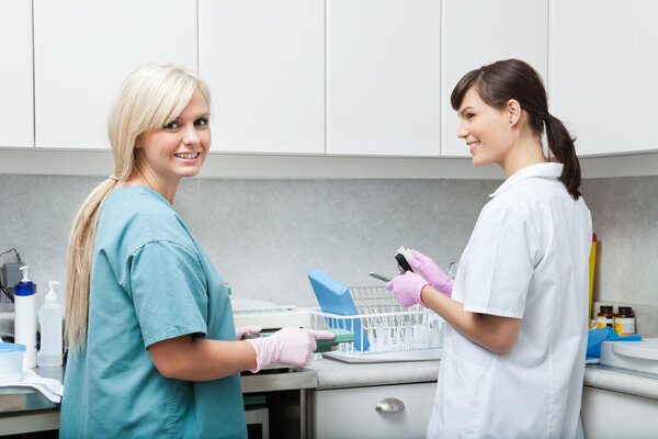 Smiling Dentist With Assistant Cleaning Medical Instruments At C