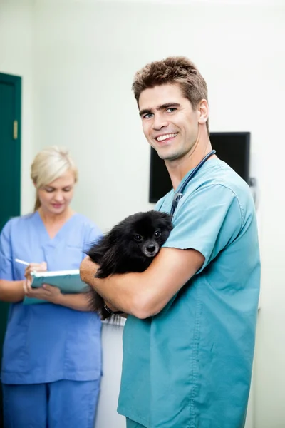 Veterinär läkare bär en hund med kvinnlig sjuksköterska skriva på — Stockfoto