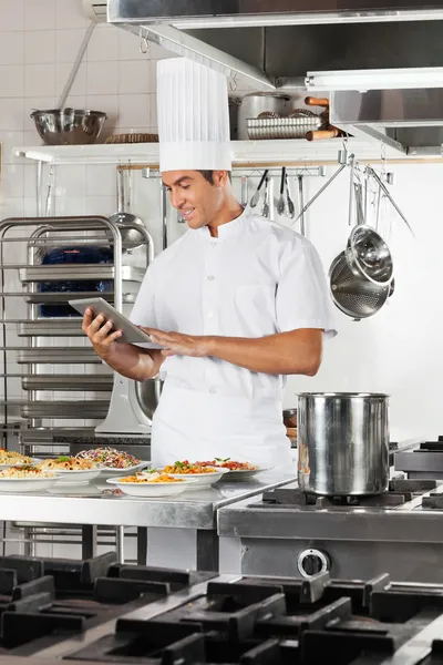 Счастливый шеф-повар с помощью цифрового планшета на кухне — стоковое фото