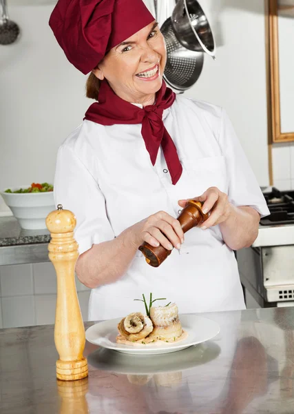 Köchin würzt Gericht mit Pfeffermühle — Stockfoto