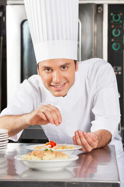 Gelukkig mannelijke chef-kok beregening specerijen op schotel — Stockfoto