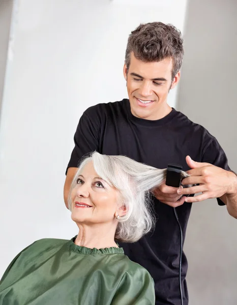 Peluquero alisando el cabello de la mujer mayor —  Fotos de Stock