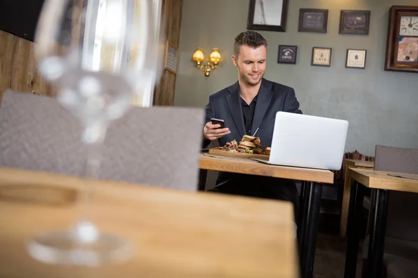 Geschäftsmann mit Laptop und Handy beim Essen — Stockfoto