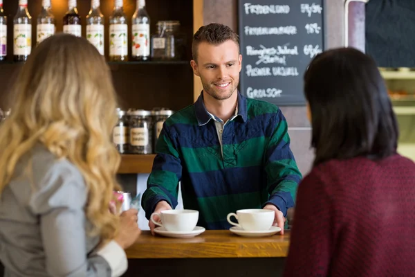 Barman serveren koffie aan vrouwelijke vrienden bij café — Stockfoto