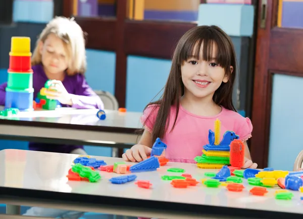 Ragazza con costruzione blocco mentre amico giocare in background — Foto Stock