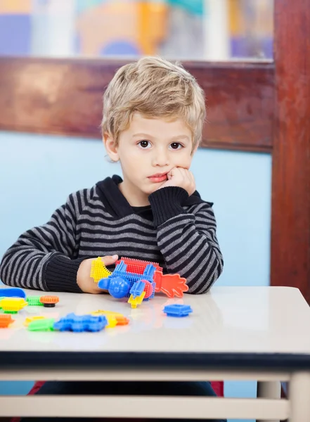 Скучный мальчик держит блоки, сидя за столом в классе — стоковое фото