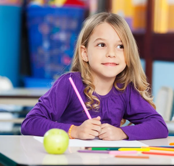 Fille réfléchie avec stylo croquis et papier dans la salle de classe — Photo