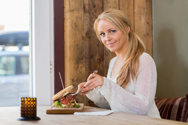 Mladá žena jíst sendvič v kavárně — Stock fotografie
