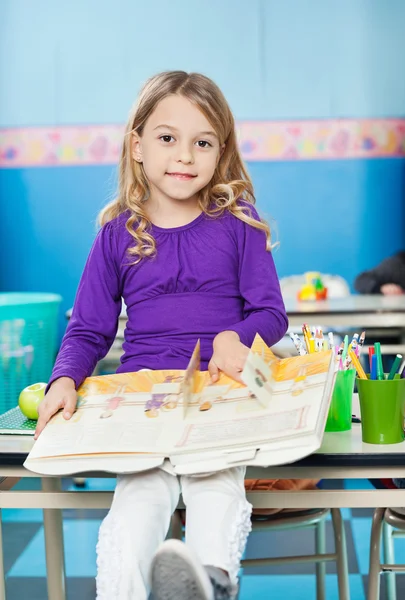 Meisje met boek zit op Bureau in klas — Stockfoto