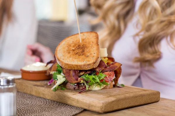 Сэндвич на деревянной тарелке с женщинами на заднем плане — стоковое фото