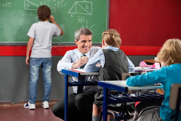 Professeur regardant écolière tout en s'accroupissant au bureau — Photo