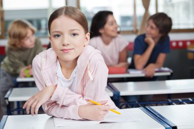 arka planda öğrencilerle masa üzerine eğilerek kız öğrenci