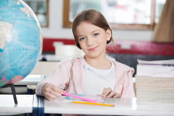 Schoolmeisje lachend met boeken en globe aan balie — Stockfoto