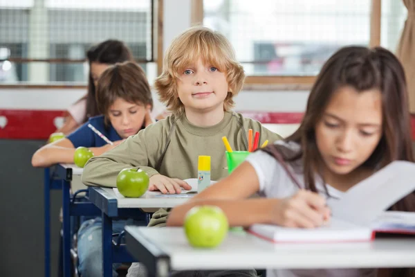 Skolpojke sitter vid skrivbord med klasskamrater i rad — Stockfoto