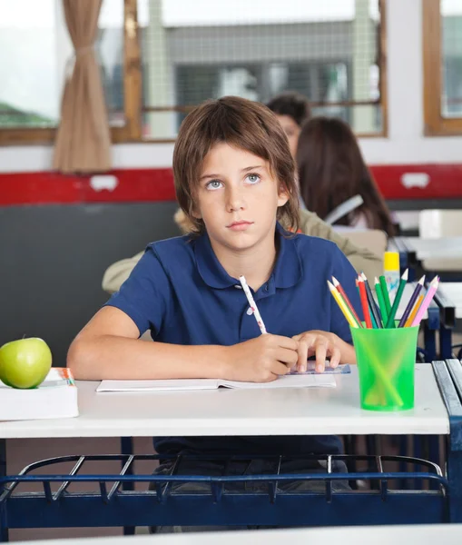 Schoolboy Looking Away While Writing At Desk — Stock Photo, Image