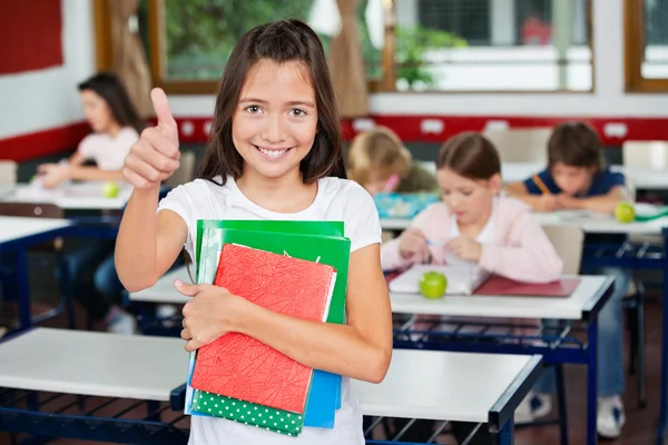 Schoolgirl Gesturing Thumbs Up While Holding Books — Stock Photo, Image