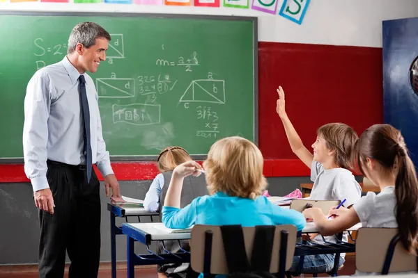 Professeur regardant écolier levant la main — Photo