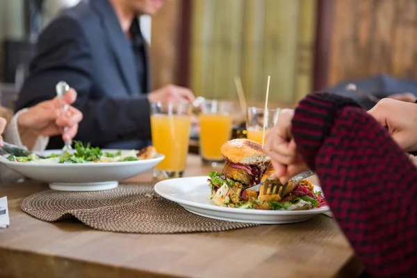 Νεαρή γυναίκα έχοντας burger με τους συναδέλφους στο café — Φωτογραφία Αρχείου