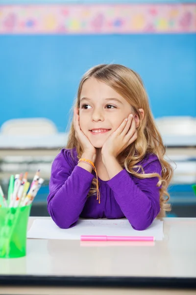 Dívka s úsměvem zatímco sedí s hlavou v ruce na stůl — Stock fotografie