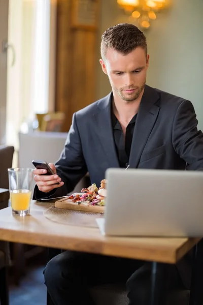 Empresario con teléfono celular y computadora portátil en restaurante — Foto de Stock