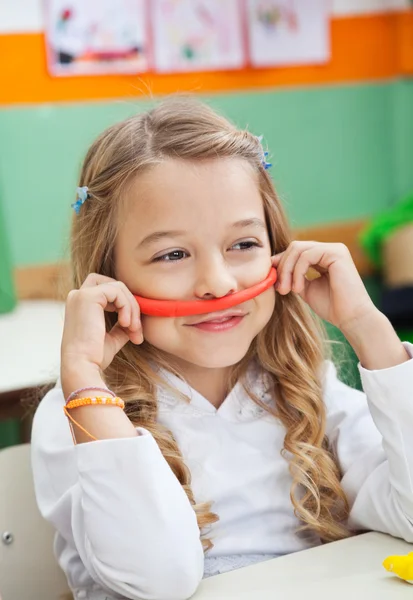 Flicka håller mustasch gjorda av lera i klassrummet — Stockfoto