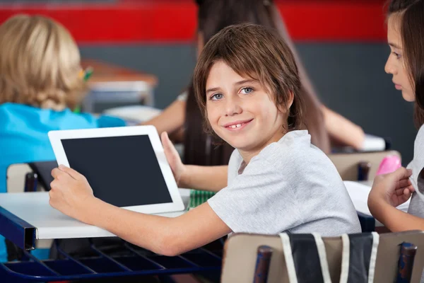 Lindo colegial sosteniendo tableta digital en el aula — Foto de Stock