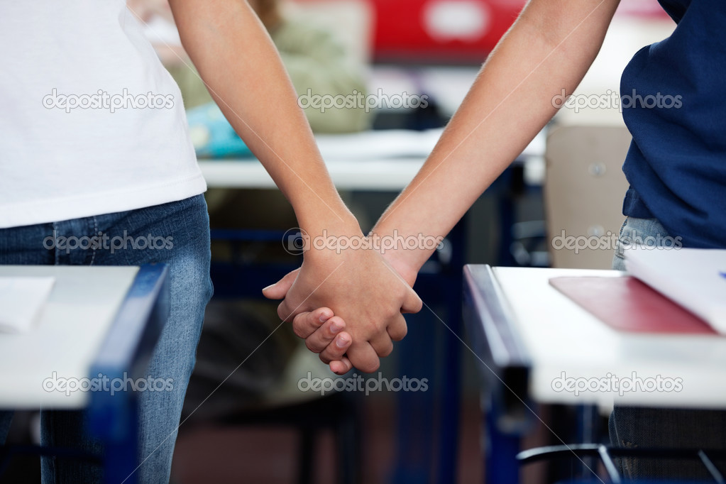 Midsection Of Schoolboy And Girl Holding Hands At Desk