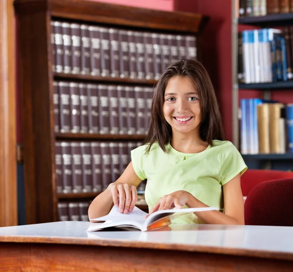 Felice studentessa con libro seduta a tavola in biblioteca — Foto Stock