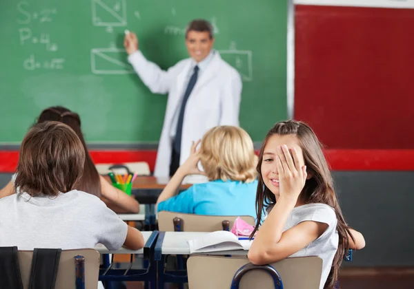 Mädchen bedeckt ein Auge, während sie am Schreibtisch im Klassenzimmer sitzt — Stockfoto