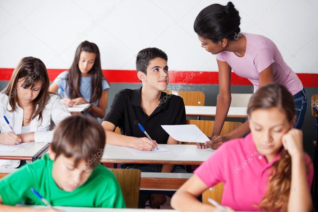 Teacher Assisting Teenage Boy During Examination In Classroom