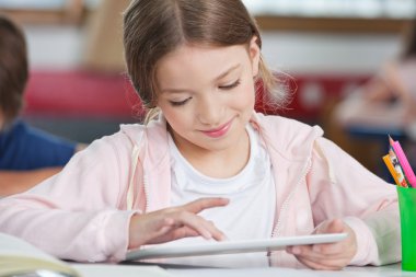 Masa başında tablet kullanırken gülümseyen kız öğrenci