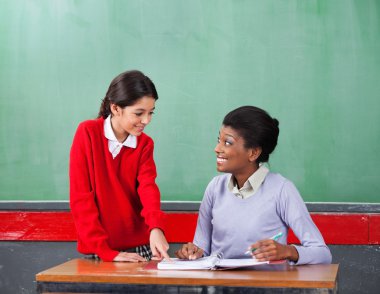 Ona bakarken öğretmen ise kağıt üzerinde işaret eden kız öğrenci