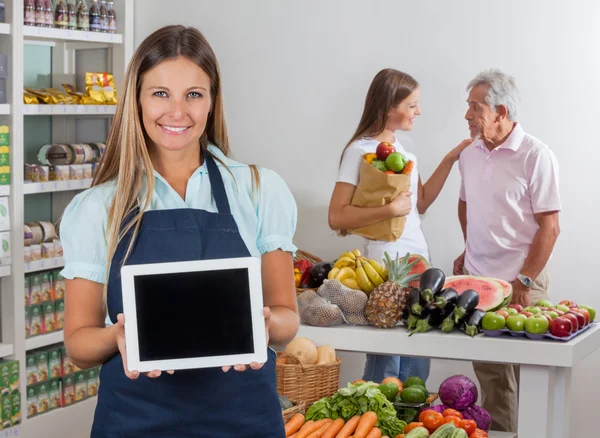 Verkoopster Tablet PC weergeven met klanten in achtergrond — Stockfoto