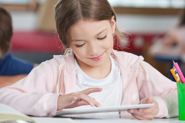 Skolflicka leende medan du använder Tablet PC på skrivbordet — Stockfoto