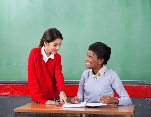 指向同时老师看着她的纸上的女学生 — 图库照片