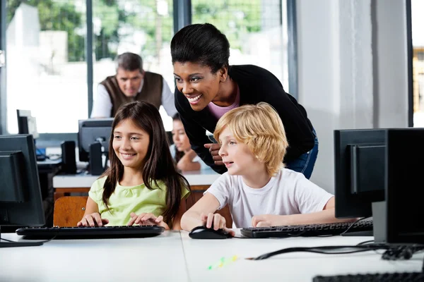 Felice insegnante assistere gli scolari nell'utilizzo del computer — Foto Stock