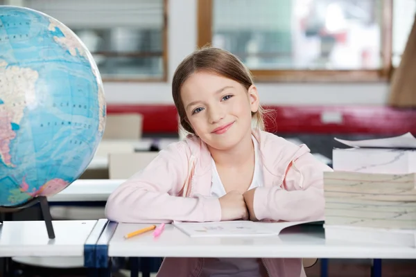 Linda colegiala sonriendo con globo y libros en el escritorio —  Fotos de Stock