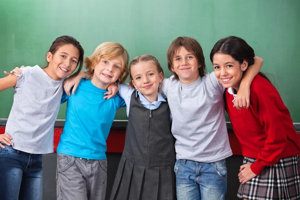 Carino scolari con braccia intorno in piedi insieme in classe — Foto Stock