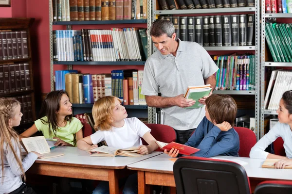 Professor se comunicando com os alunos sentados na mesa na biblioteca — Fotografia de Stock