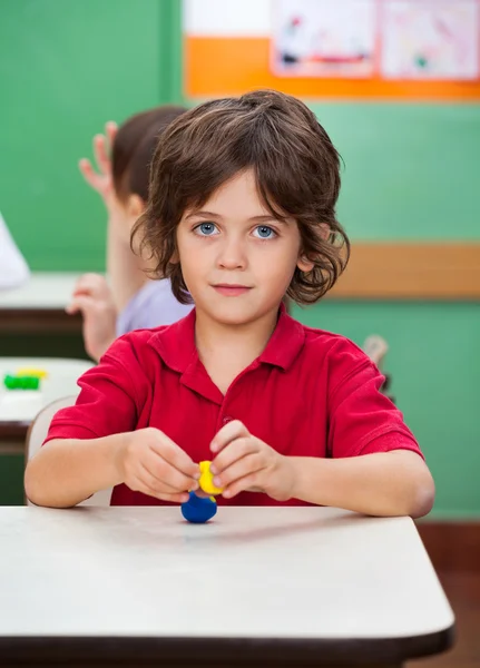 Niño sosteniendo modelo de arcilla en el escritorio — Foto de Stock