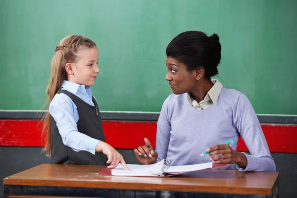 Lehrerin lächelt, während sie Schulmädchen im Klassenzimmer ansieht — Stockfoto