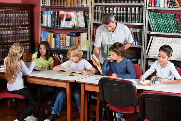 Leraar weergegeven: boek naar schooljongen in bibliotheek — Stockfoto